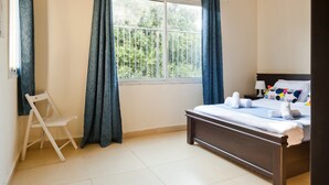 A bedroom with a bed, a chair, a window with curtains, and a view of trees outside. - NHE Rothschild Allenby Apartments (Tel Aviv)