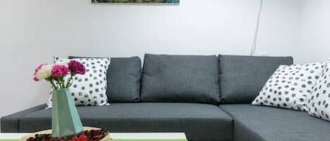 A grey sofa with polka dot pillows, a vase with flowers, and a painting on the wall.