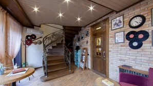 A cozy interior with a wooden staircase, a brick wall with framed pictures, and a clock. - Sacvoyage Hotel (Almaty)