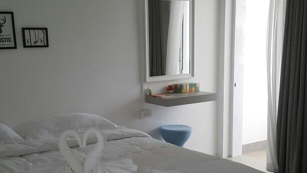 A hotel room with a large bed, a blue stool, a mirror, and a window with curtains. - Patchy&PPraw Family (Ubon Ratchathani)