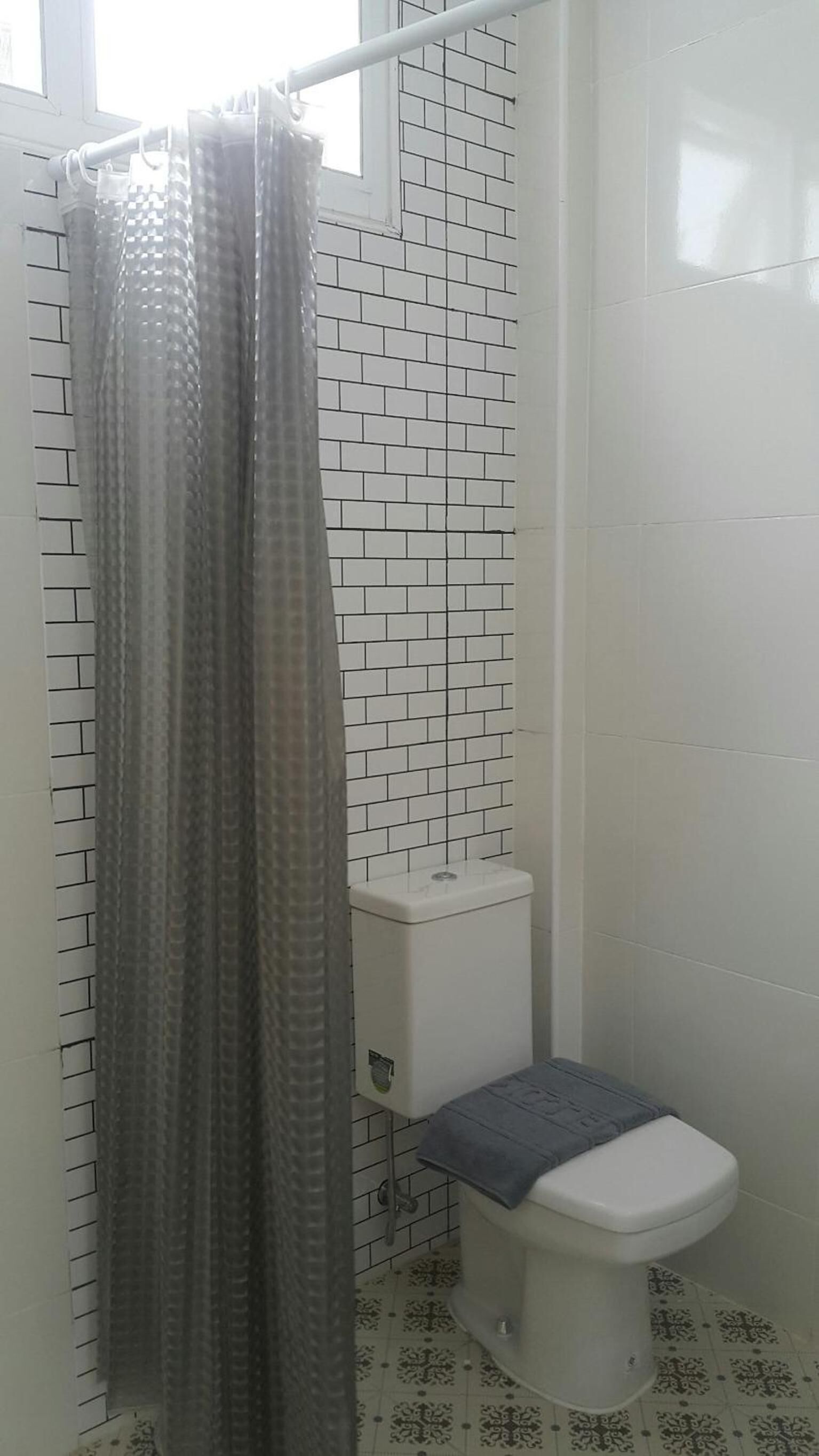 A bathroom with a toilet, a shower curtain, and patterned tiles on the walls.