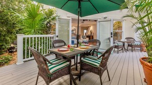 Une terrasse extérieure avec une table et des chaises, entourée de plantes et d’une clôture blanche.