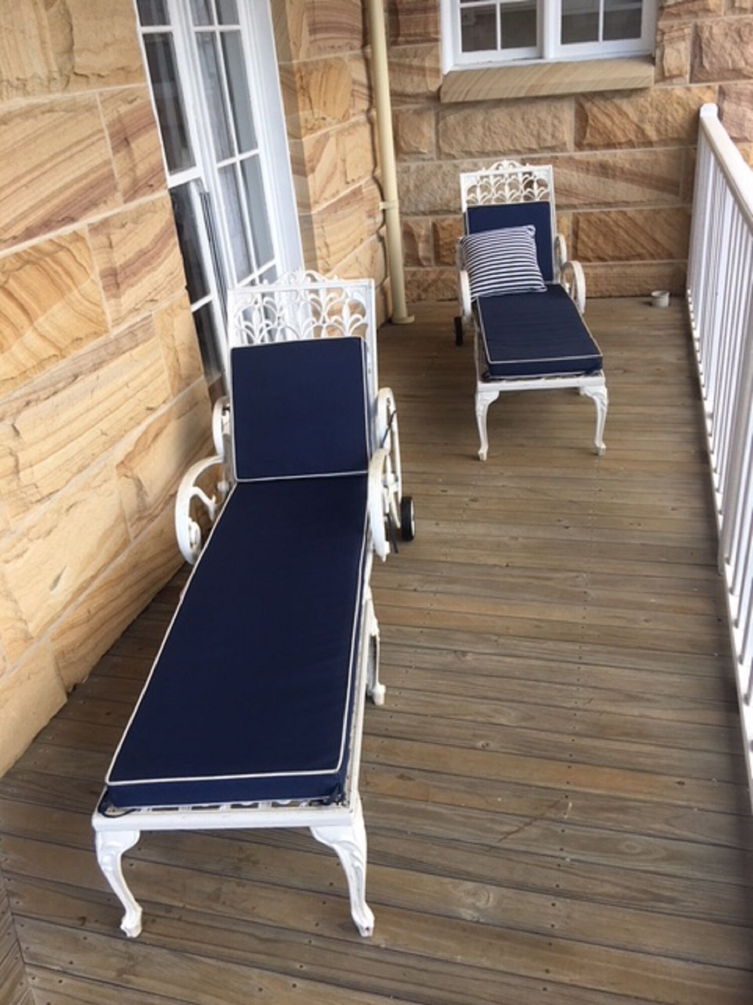 Une terrasse en bois avec deux chaises longues à l’assise blanche et aux coussins foncés.