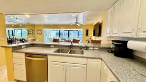 A kitchen with granite countertops, white cabinetry, a built-in dishwasher, and a coffee maker.