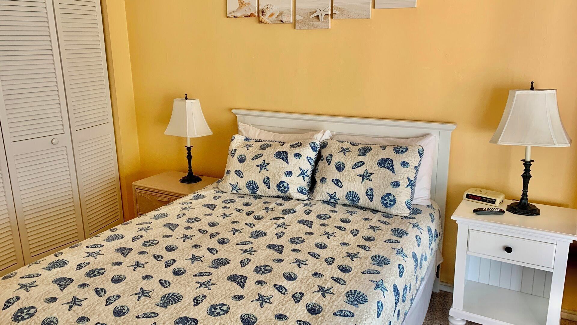 A bed with a patterned bedspread, two bedside tables with lamps, a nightstand, and a wall with framed pictures.