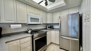 A modern kitchen with white cabinetry, a stainless steel refrigerator, a microwave, a stove, and a kettle. - Love to Boat, Kayak or Canoe? Then this Mariner Pointe waterfront condo is for you!  Bring Your Boat! (Sanibel)