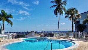 A pool area with a clear view of the ocean, surrounded by palm trees and a white fence.