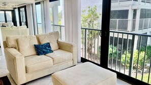A beige sofa with a blue pillow, a matching ottoman, and a view of a balcony with a railing.