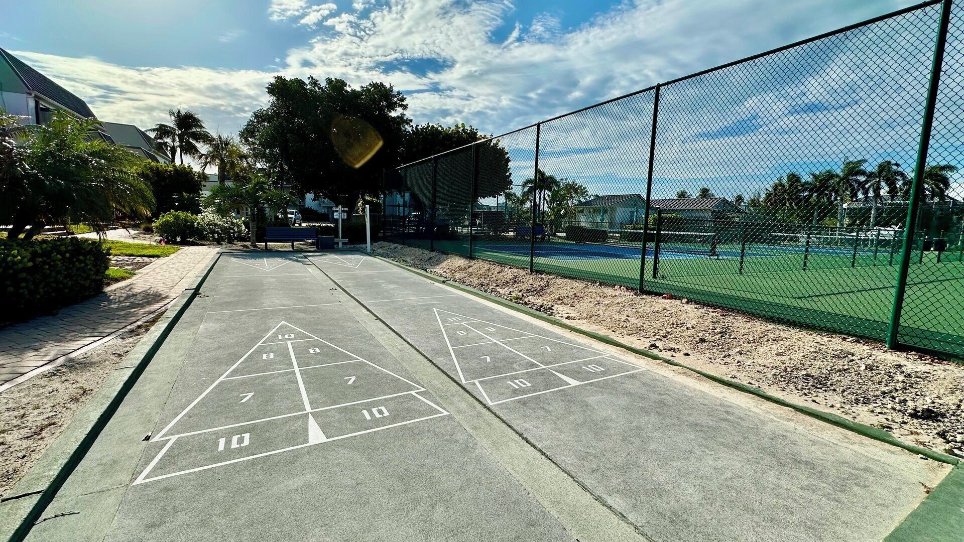 Un court de tennis avec un filet, entouré d’une clôture, et un terrain de jeu de shuffleboard au premier plan.