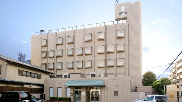 Un hôtel à plusieurs étages, doté d’une façade carrelée, d’une entrée imposante surmontée d’un auvent vert et d’un panneau indiquant un espace de stationnement.