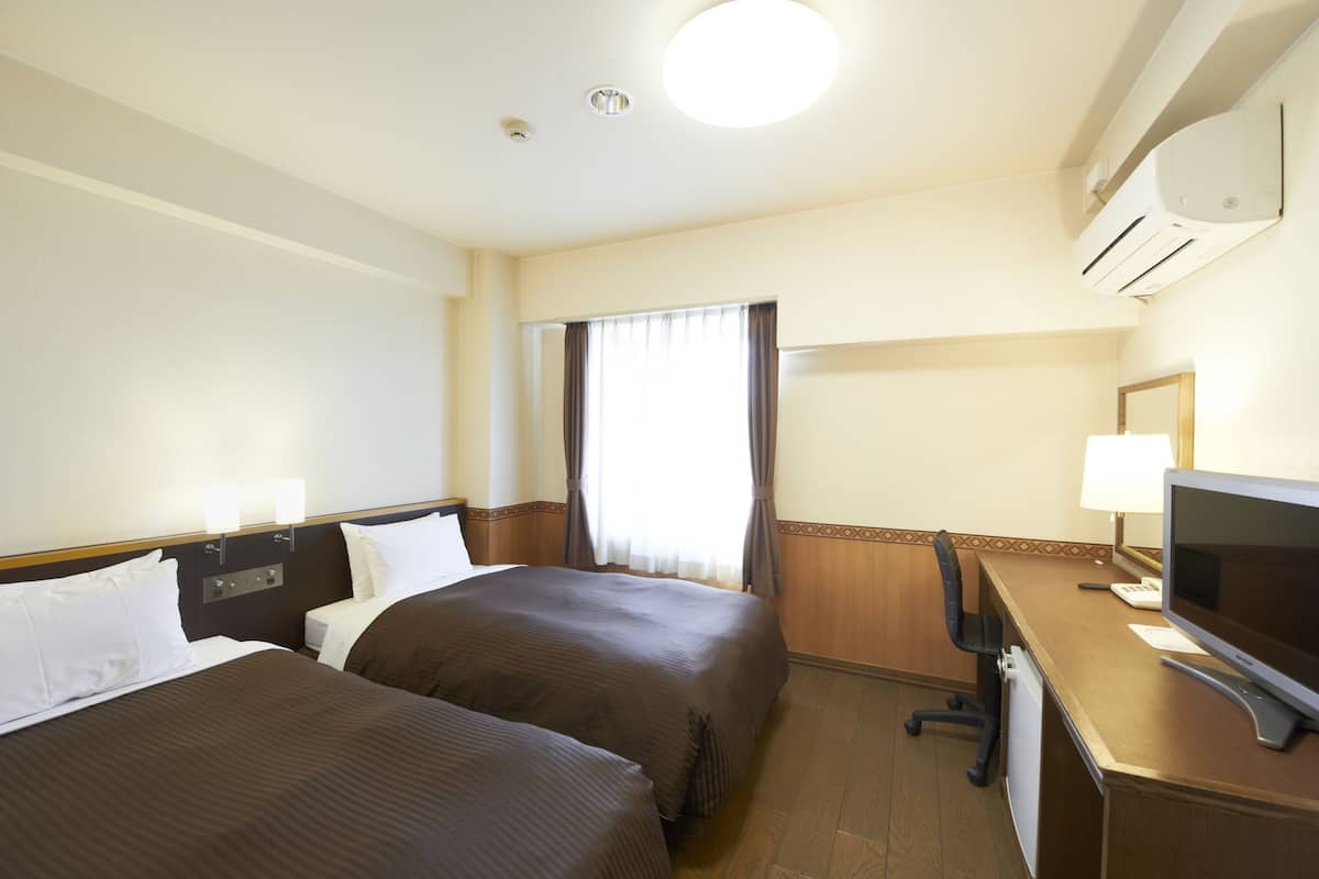 Habitación de hotel con dos camas, un escritorio con ordenador y una ventana con cortinas.