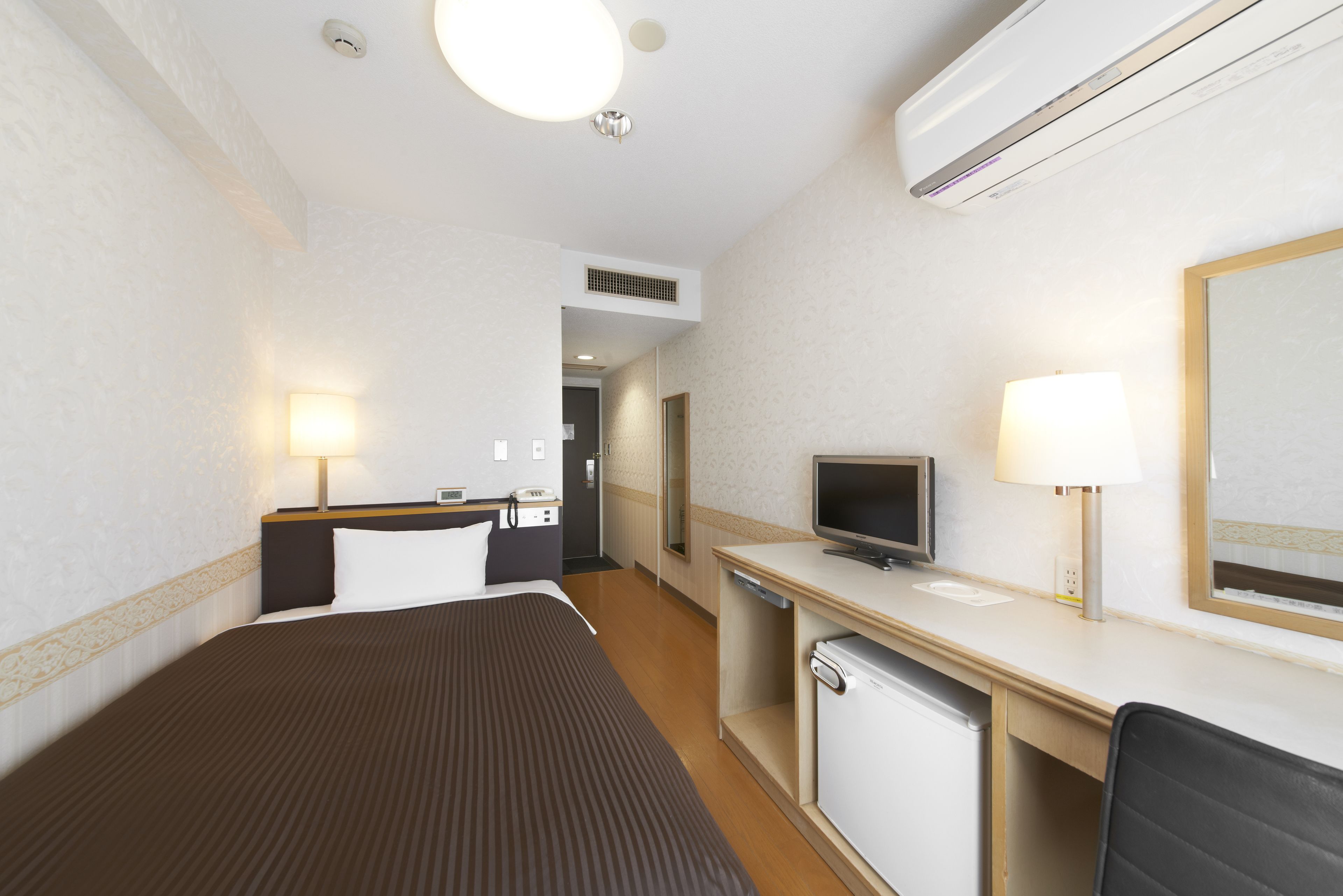 A hotel room with a bed, desk, television, and a mirror.