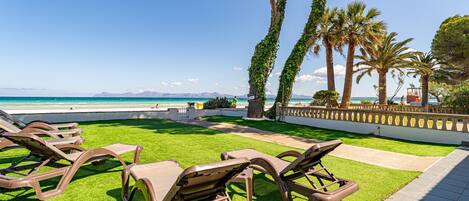 Un espace de détente aménagé au bord de la plage, avec des chaises longues, des palmiers et une vue sur la mer.