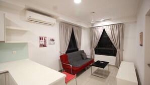 Un espacio habitable compacto con kitchenette, un sofá rojo, una mesita y una ventana con cortinas.
