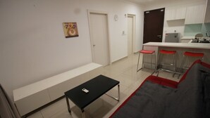 Un espacio habitable compacto con kitchenette, una zona de comedor con taburetes de bar y una sala de estar con sofá y una mesita.