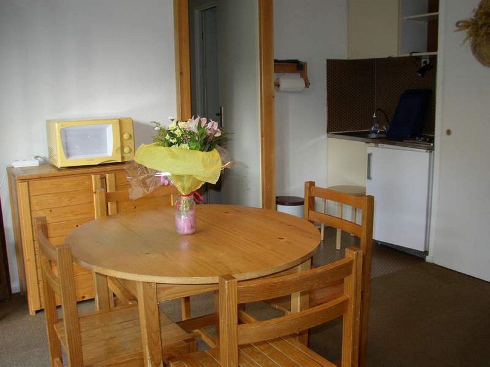 A small dining area with a wooden table, chairs, a microwave, and a bouquet of flowers.