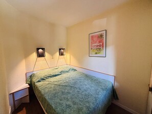 A small, neatly arranged bedroom with a bed, two wall-mounted lamps, and a framed picture on the wall.