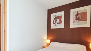 Une chambre d’hôtel avec un lit, deux lampes fixées au mur et deux œuvres d’art encadrées.