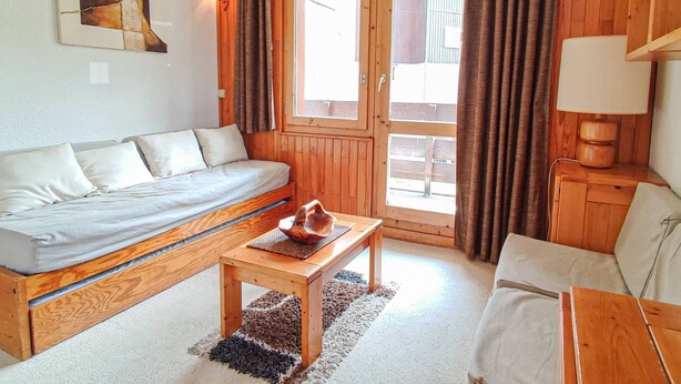 Une pièce avec un canapé en bois, une petite table en bois, une lampe et une fenêtre avec des rideaux.