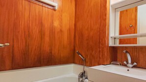 Une salle de bain avec un mur en bois, une baignoire blanche et un lavabo surmonté d’un miroir.