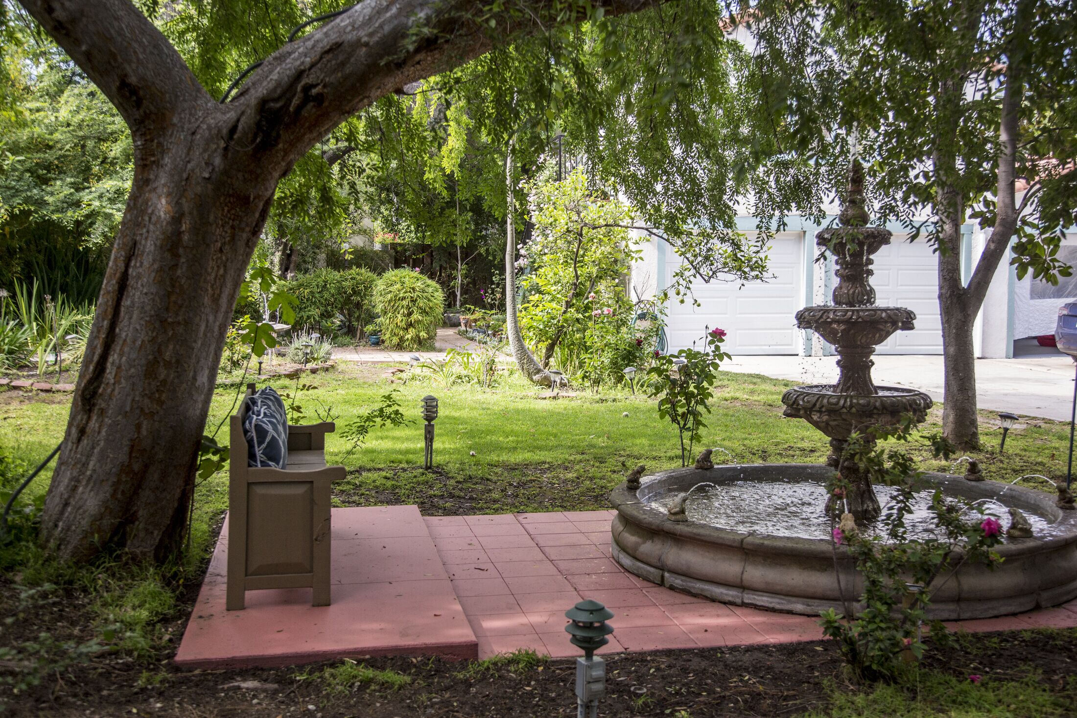 Un jardín con una fuente de piedra, un banco y un árbol.