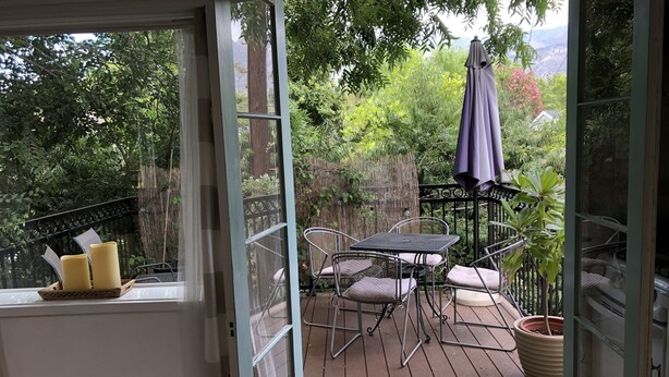 Eine Terrasse mit Tisch, Stühlen, einem Blumentopf und einem Fenster mit Vorhängen.
