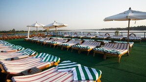 A sun deck with rows of lounge chairs and umbrellas, a green carpet, and a view of the water. - Nile Carnival Cruise (Luxor)