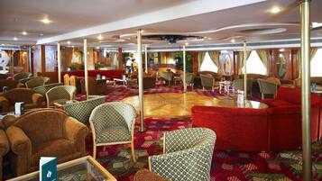 Un vaste espace de détente doté de nombreux sièges, notamment des canapés et des fauteuils, disposés autour d’un tapis central à motifs.