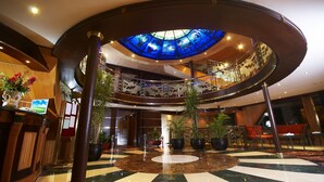 A hotel lobby with a central circular area, a glass ceiling with a blue tint, and a check-in counter with a computer monitor. - Nile Carnival Cruise (Luxor)