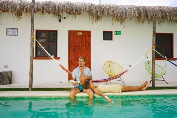 A couple relaxing in a pool with a hammock, a wooden door, and a thatched roof. - Kinta Kan Boutique Hotel (Cozumel)