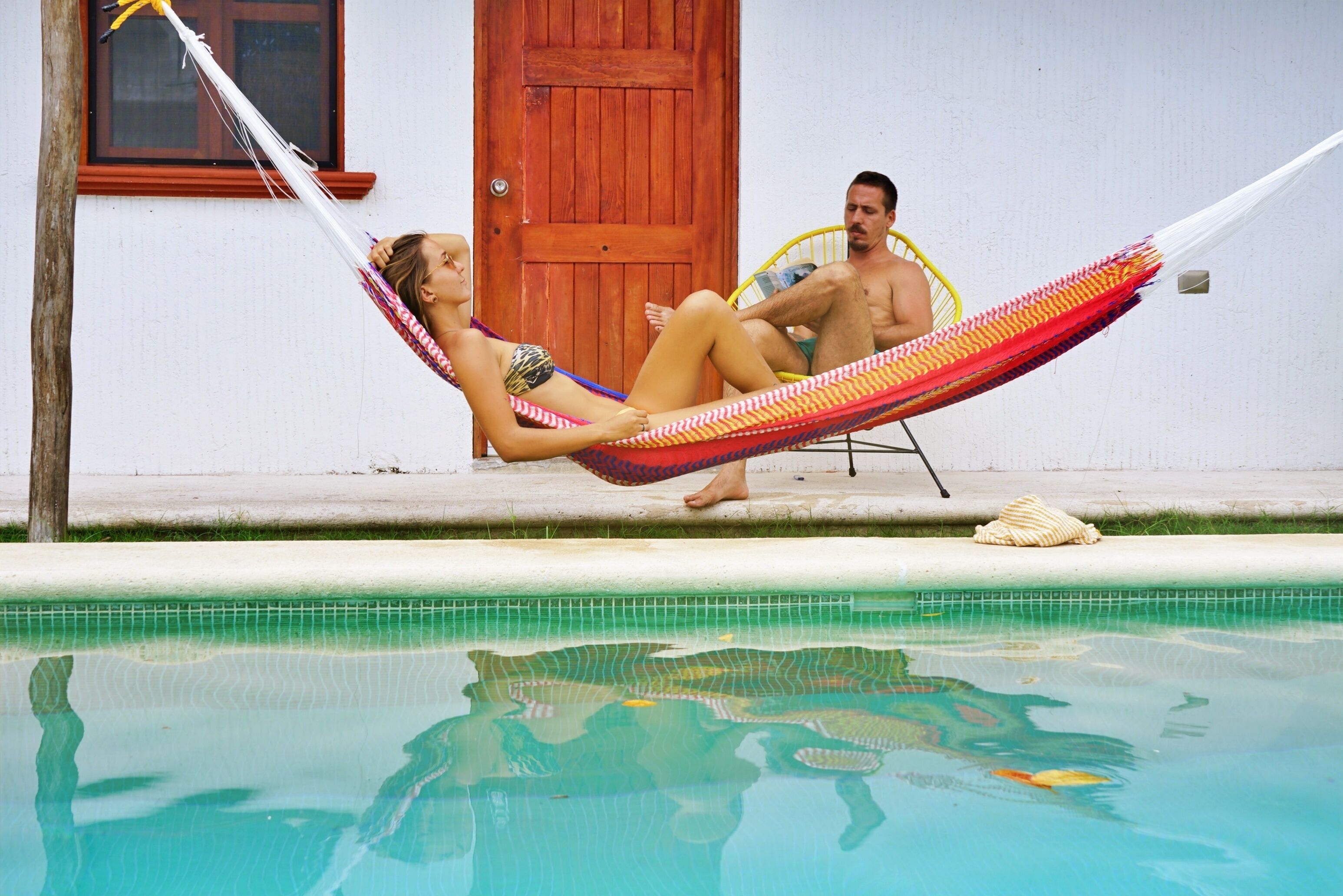 A poolside area with a hammock, a wooden door, and a tiled pool.