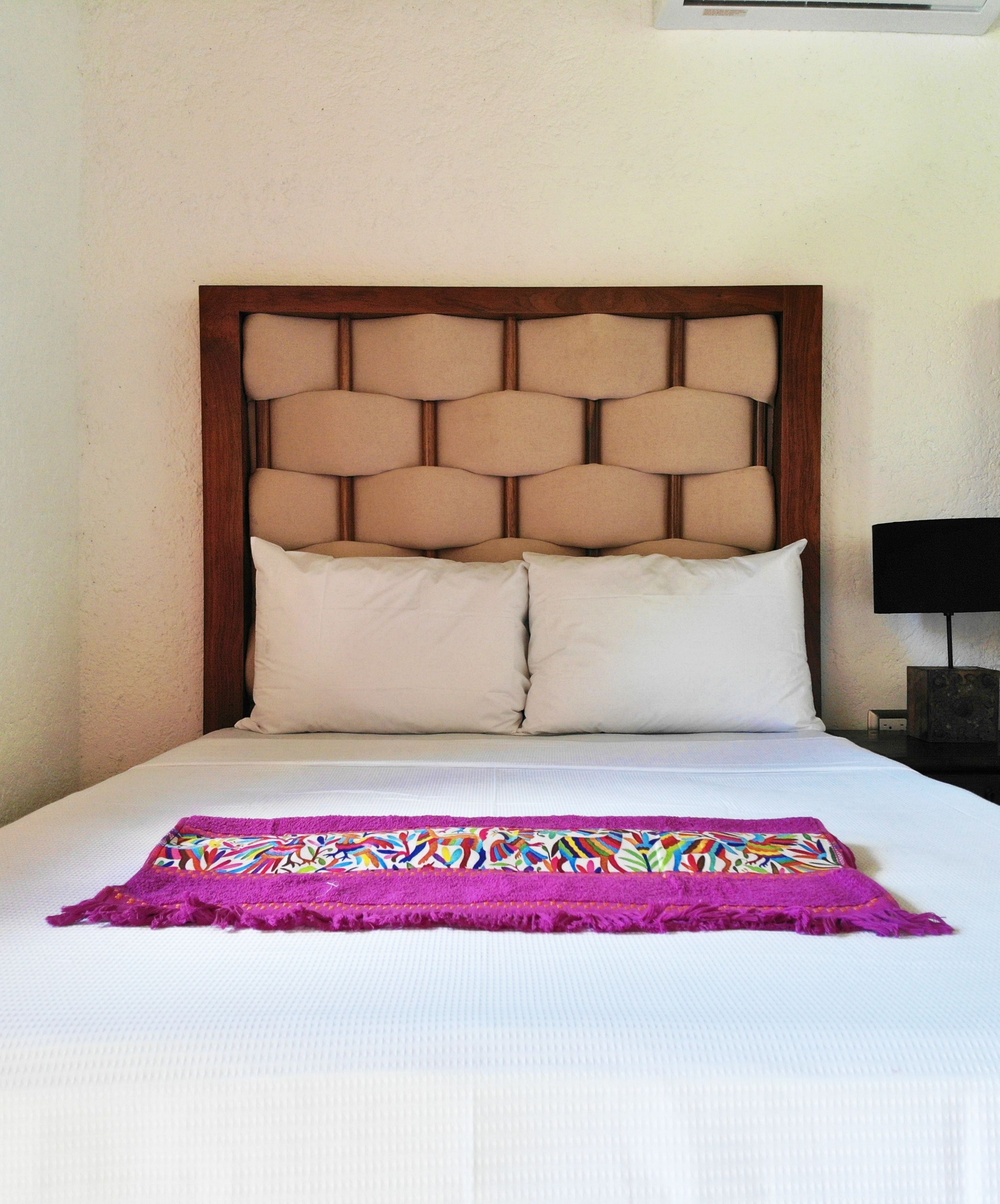 Una cama con cabecera de madera, dos almohadas blancas y una manta colorida.