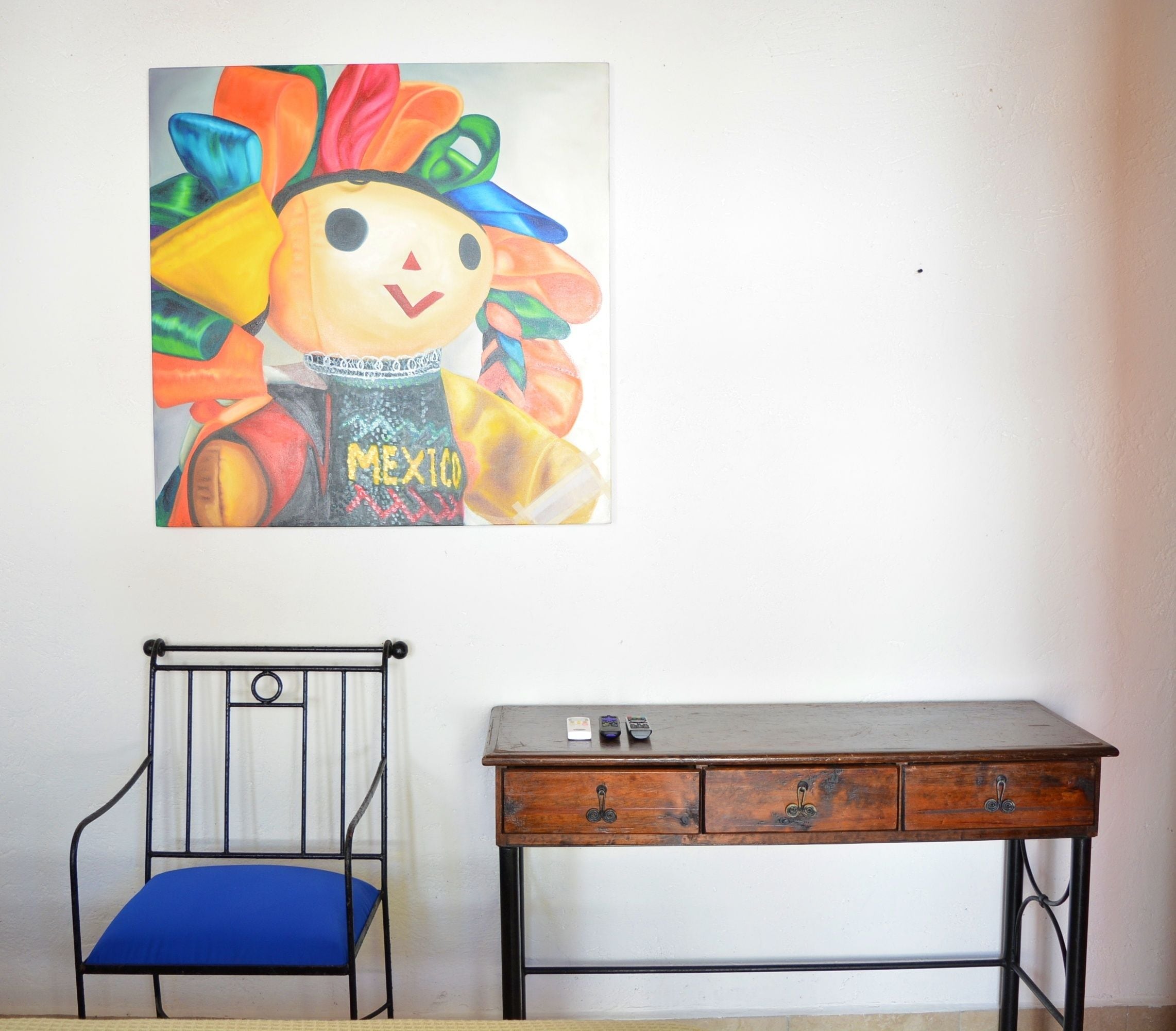 A room with a metal chair, a wooden desk, and a colorful painting on the wall.