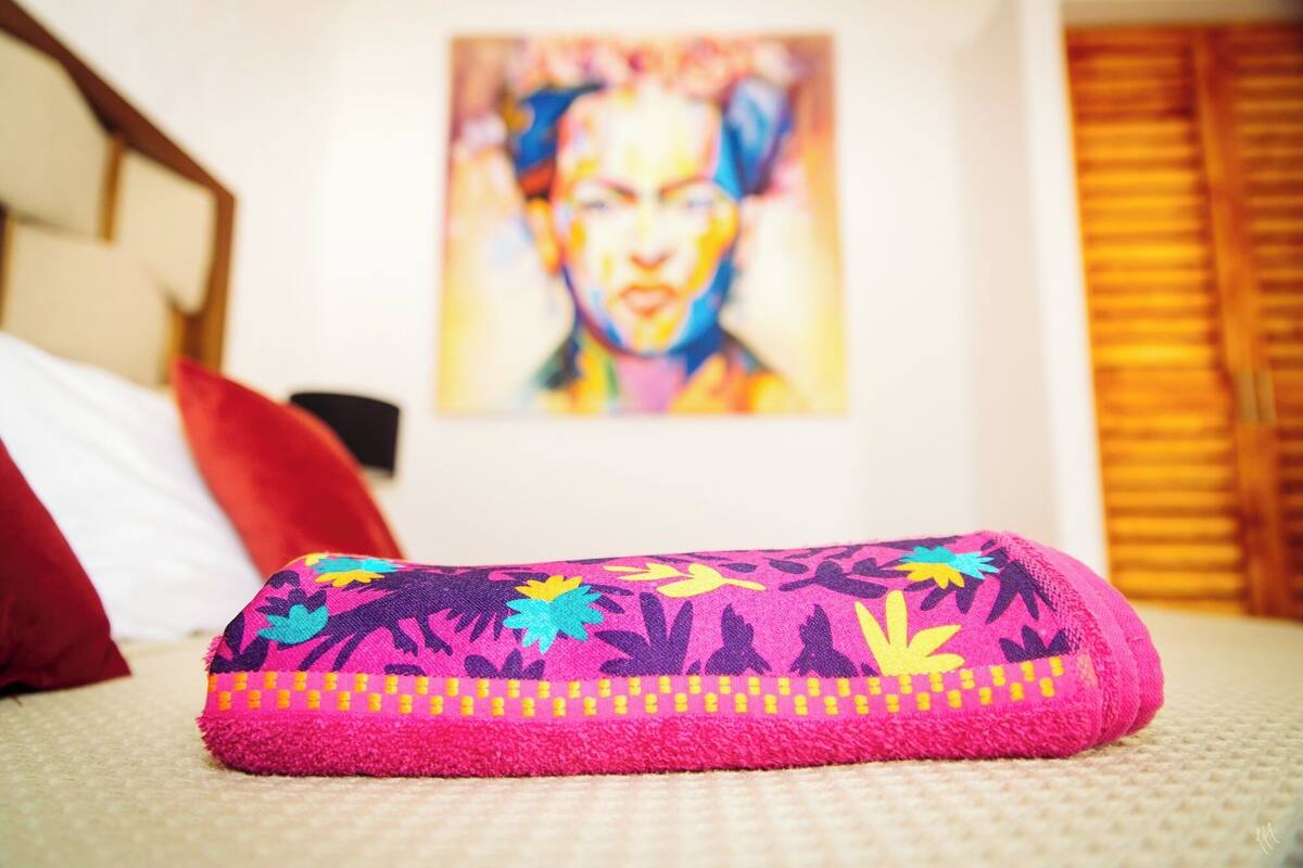 Una cama con una toalla colorida, un cuadro en la pared y una ventana con persianas.
