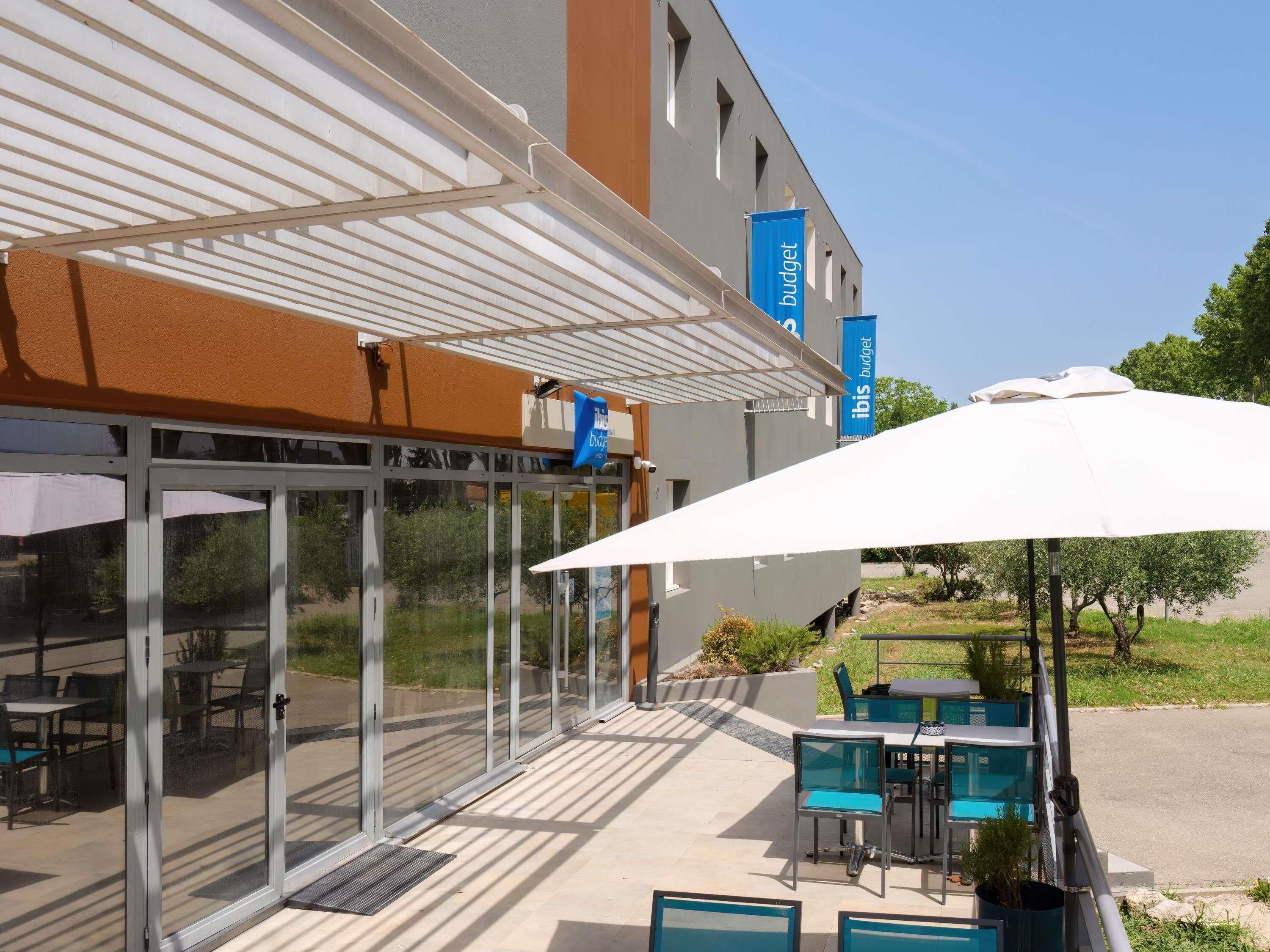 Exterior de un hotel con un porche cubierto, mobiliario al aire libre y vistas despejadas del entorno.