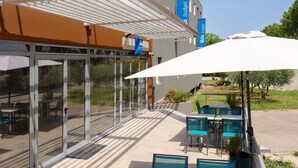 A hotel exterior with a covered patio, outdoor seating, and a clear view of the surrounding area. - ibis budget Pertuis Portes du Luberon (Pertuis)