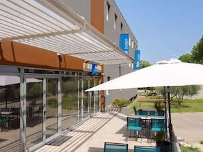 A hotel exterior with a covered patio, outdoor seating, and a clear view of the surrounding area. - ibis budget Pertuis Portes du Luberon (Pertuis)