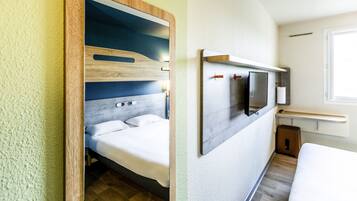 Een moderne slaapkamer in een camper met een bed, een wandtelevisie en een klein krukje.