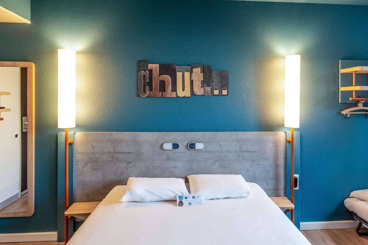 A hotel room with a bed, two bedside tables, a headboard, and a wall-mounted sign.
