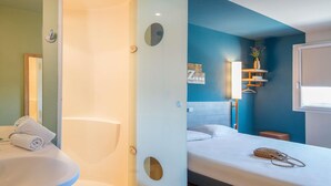 A modern hotel room with a bathroom, a bed with a headboard, a bedside table, and a window. - ibis budget Pertuis Portes du Luberon (Pertuis)