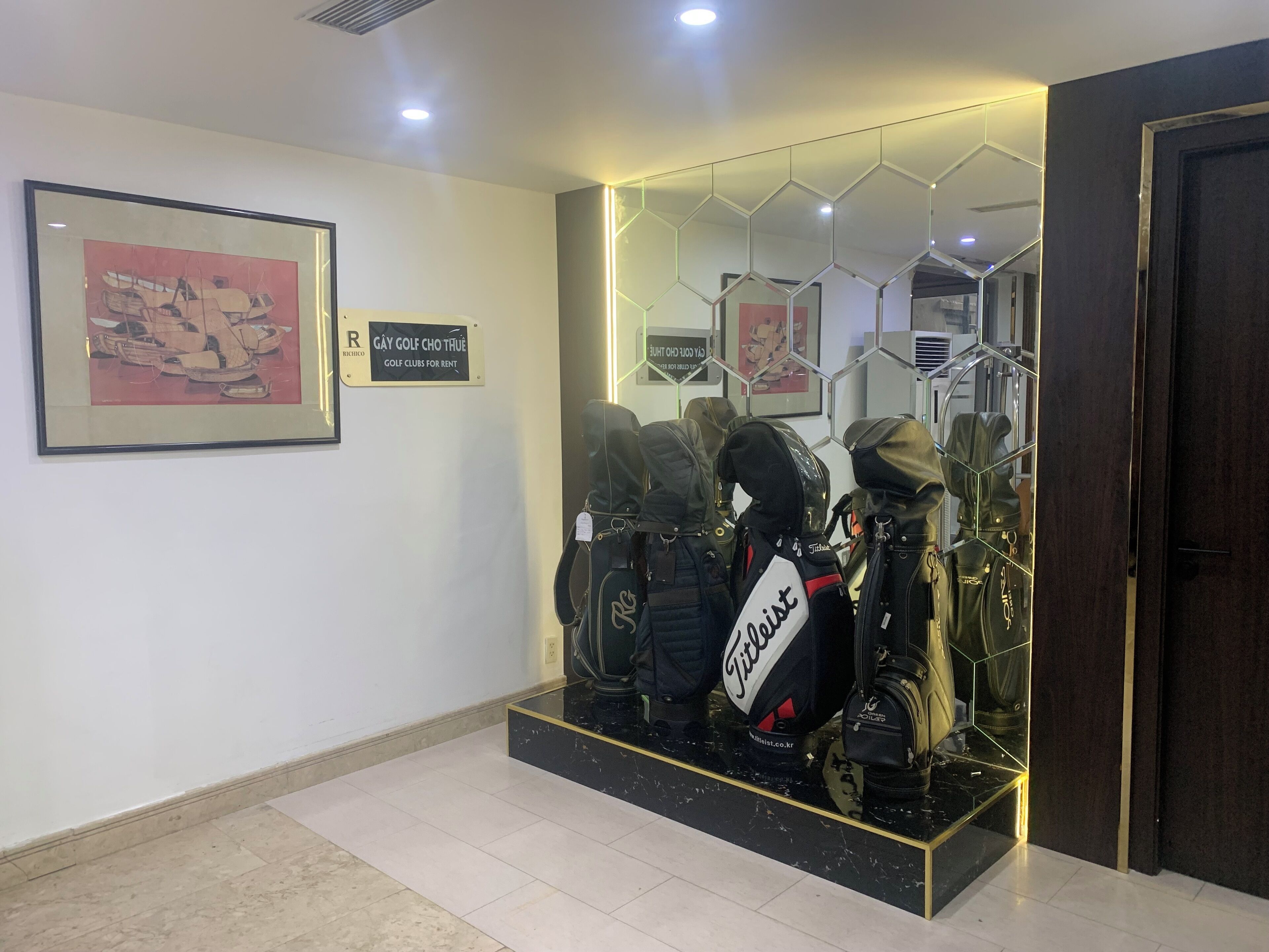 A reception area with a framed artwork, a sign for gay golf clubs, and a display of golf bags.