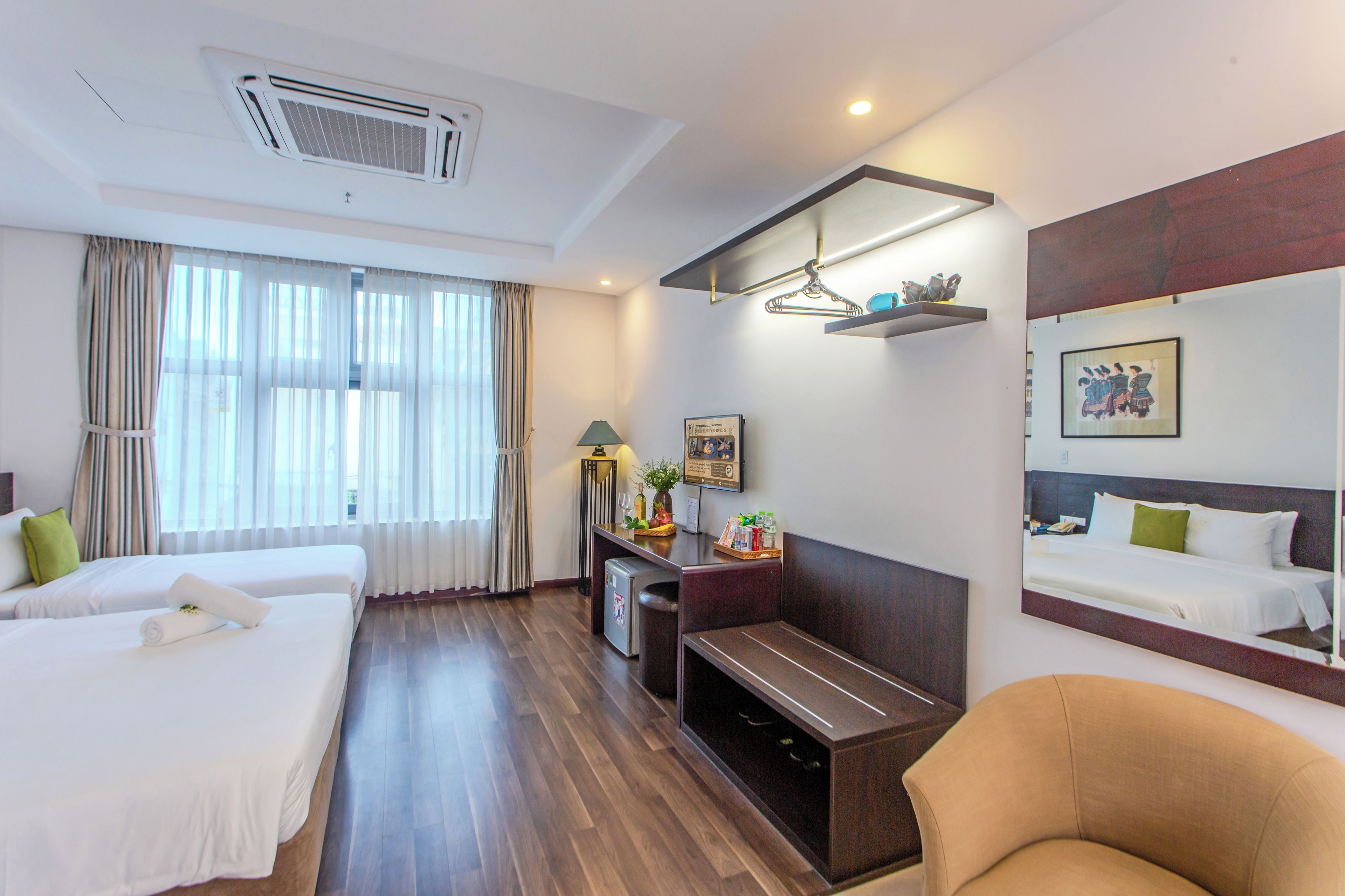 A hotel room with two beds, a desk, a chair, a TV, and a mirror.
