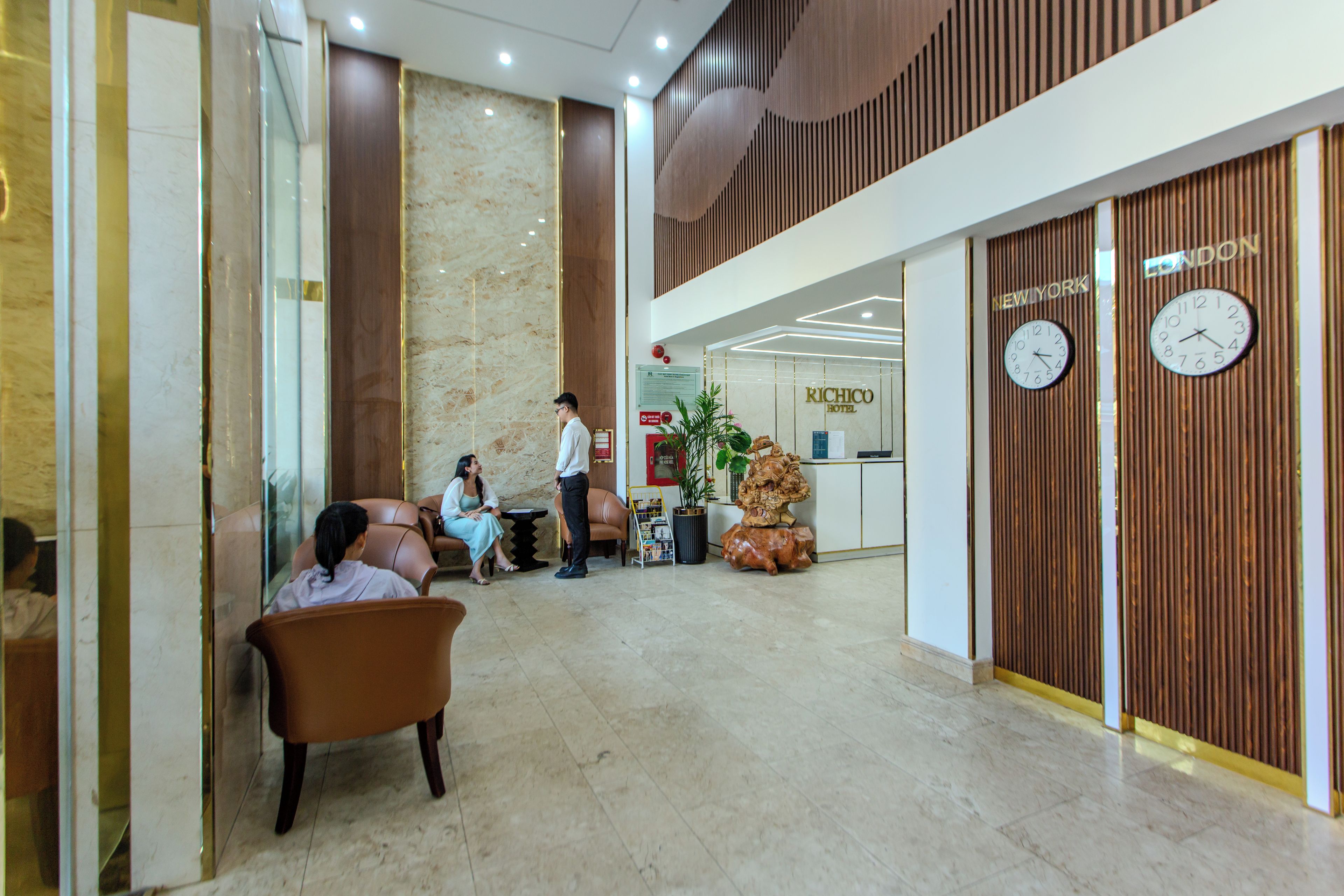 A hotel lobby with a reception desk, seating area, and clocks displaying 'New York' and 'London' times.
