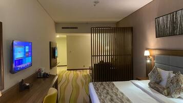 A hotel room with a bed, a desk with a computer, a TV, and a view of a room with a wooden partition.