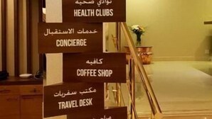 A hotel reception area with a signpost indicating guest rooms, reception, health clubs, concierge, coffee shop, travel desk, and toilets. - Jacob's Garden Hotel (Dubai)