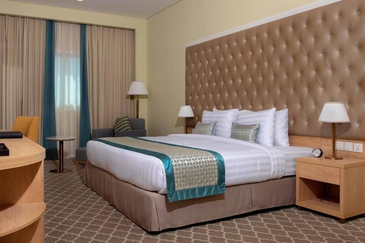 A hotel room with a large bed, two bedside tables, a chair, a desk, and a window with curtains.