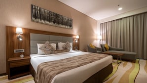 A hotel room with a large bed, a sofa, a desk, and a painting on the wall. - Jacob's Garden Hotel (Dubai)