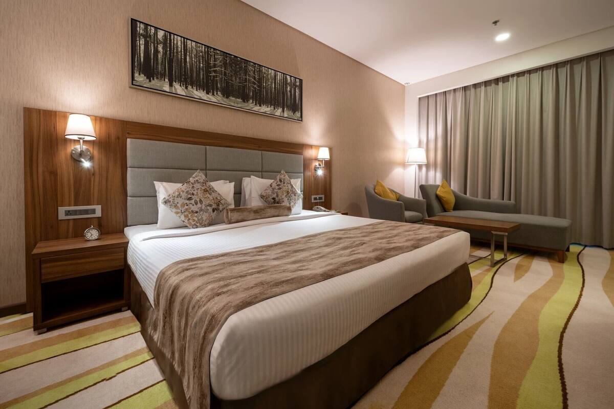 A hotel room with a large bed, a sofa, a desk, and a painting on the wall.