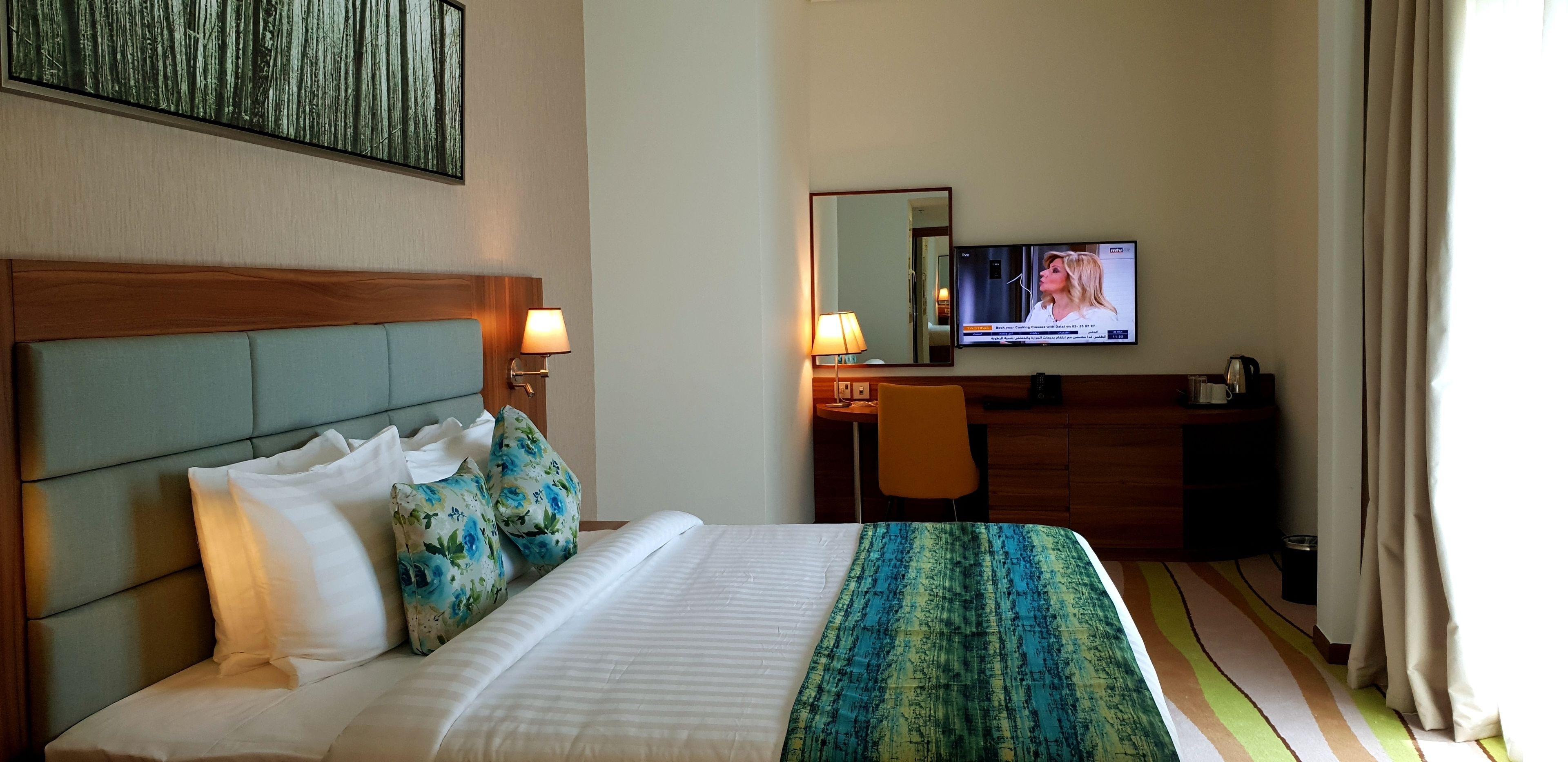 Una habitación de hotel con cama, escritorio, silla, televisor y ventana con cortinas.
