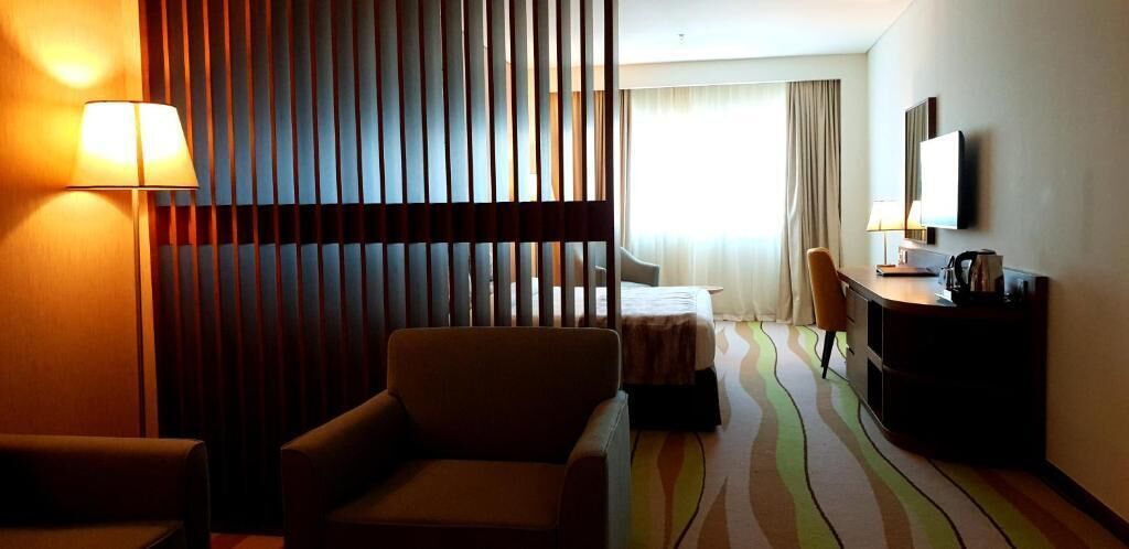 A hotel room with a bed, a desk, a chair, a lamp, and a TV.
